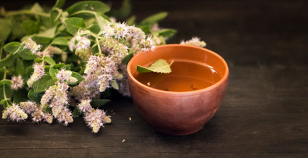 blooming mint grass with a cup of tea on a dark table.