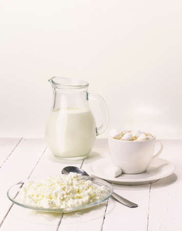 Fresh cows milk in a jug on a white background with healthy cottage cheese and a cup of coffee with marshmallowsの写真素材