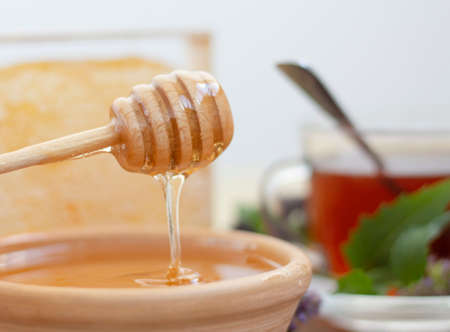 honey flows beautifully from a wooden fluted spoon against the background of honeycombs and teaの写真素材