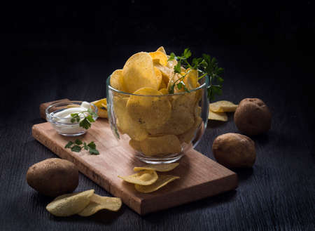 glass bowl of potato chips on a dark wooden background with sauce