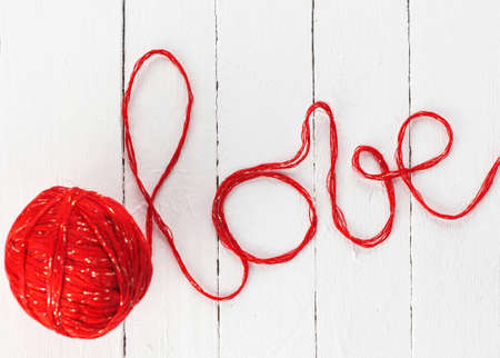 the word love, made of red yarn, is written on a white wooden background.