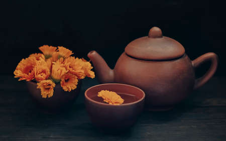 Herbal tea in a teapot and a cup of calendula flowers on a dark wood background.の写真素材