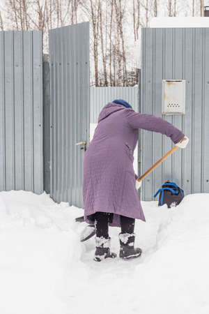 An elderly woman cleans the snow near her house in the village.の写真素材