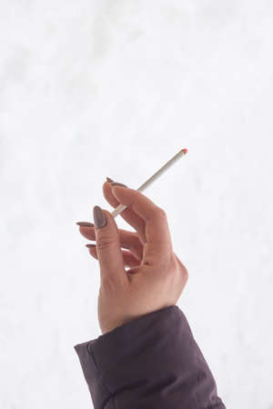 a woman's hand holding a smoking cigarette against the light background of the copy space.の写真素材