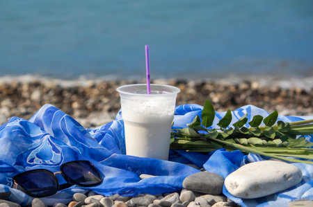 a milkshake in a disposable plastic cup with a straw On the background of the blue sea. Healthy lifestyleの写真素材