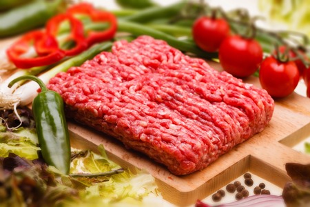raw minced meat with vegetables on wooden board, selective focusの写真素材