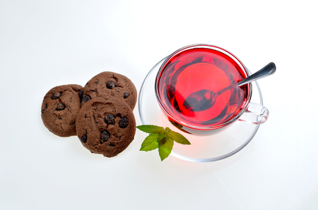 Hibiscus tea glass cup on a saucer with mint leaves, spoon and chocolate cookiesの写真素材