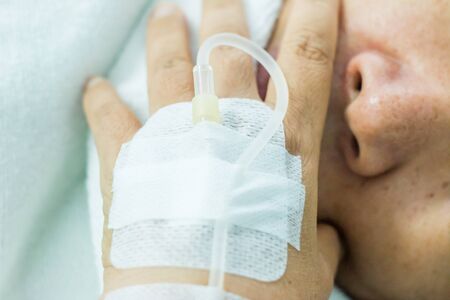 Female patient's hand recieving iv saline solution in hostpital. shoot on white bed backgroundの写真素材