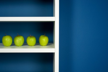 Green apple inside white bookcase in blue roomの写真素材