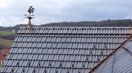 The roof is covered with black roof tiles and a weather vane on the ridgeの写真素材