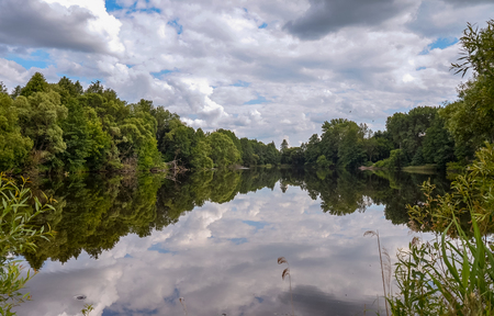 A picturesque lake among the trees. The blue sky is reflected in the mirror-like surface of the waterの写真素材