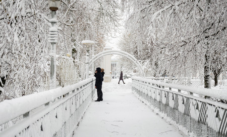 Young woman with a boy stands on a snow-covered bridge in winter in the parkの写真素材
