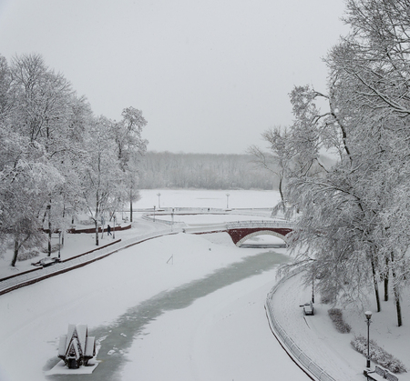 The bridge across the swan lake covered with ice and snow in the Gomel park after the snowの写真素材