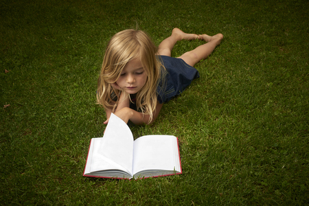 Cute Little Blond Girl Reading Book Outside on Grassの写真素材