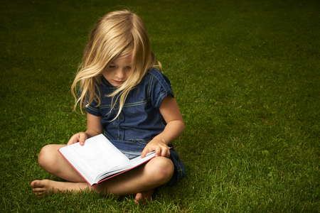 Cute Little Blond Girl Reading Book Outside on Grassの写真素材