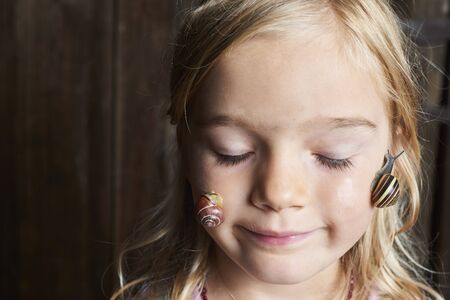 Portrait of cute blond child girl with snail on her faceの写真素材