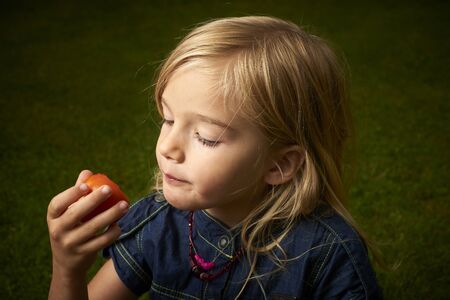 Cute blond child girl eating tomato outside in the gardenの写真素材