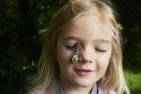 Portrait of cute blond child girl with snail on her faceの写真素材