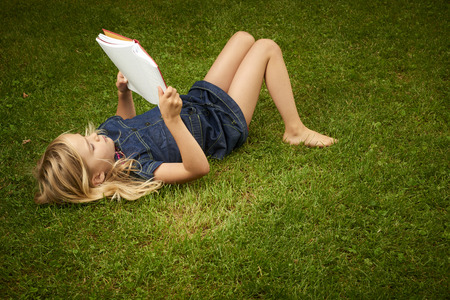 Cute Little Blond Girl Reading Book Outside on Grassの写真素材
