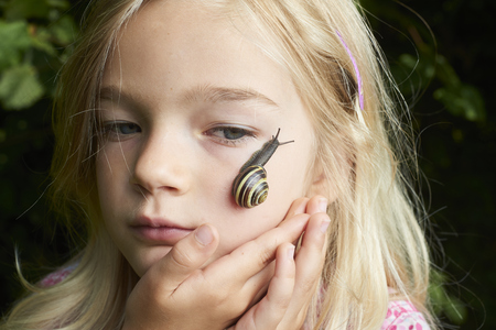 Portrait of cute blond child girl with snail on her faceの写真素材