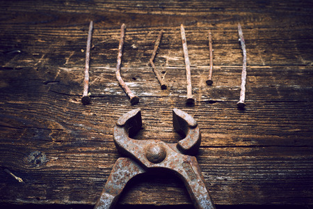 Old rusty tongs with nails on wooden boards backgroundの写真素材