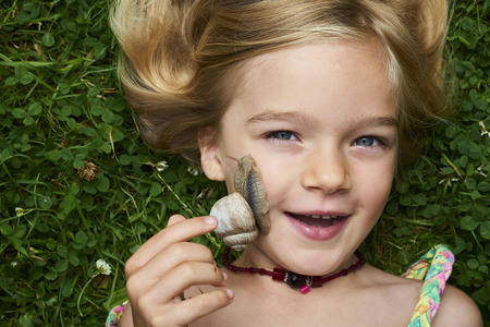 Portrait of cute blond child girl with snail on her faceの写真素材