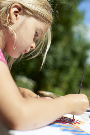 A girl painting with water colors (watercolors) painting a paper plate with watercolor paints outside in gardenの写真素材