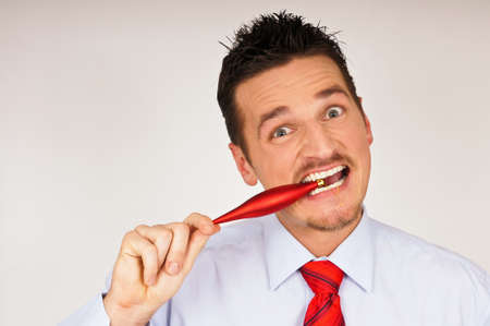 Happy young man in shirt and tie shows how bites Christmas ornamentの写真素材