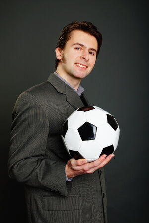 Young businessman in suit holds a soccer ball on gray backgroundの写真素材
