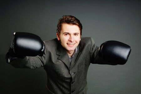 Young businessman in gray suit boxing with boxer glovesの写真素材