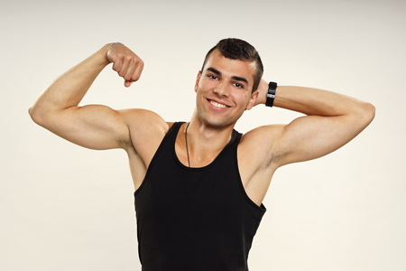 Young smiling man in black undershirt poses and shows bicepsの写真素材