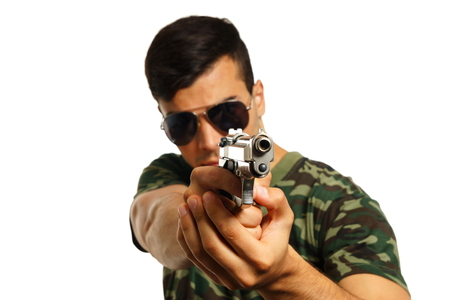 Young military man pointing a gun in hand on white background, focus is on gunの写真素材