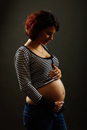Pregnant young woman caressing her belly on the gray backgroundの写真素材