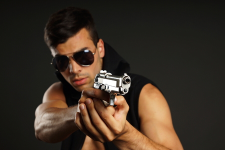Young man pointing a gun in hand, focus is on gun barrelの写真素材