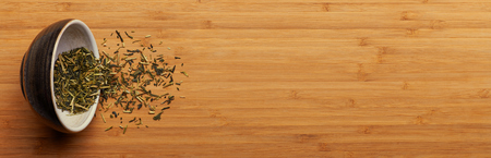 Spilled japanese kukicha green tea from cup over bamboo boardの写真素材
