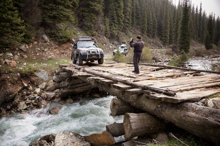 KARAKOL REGION , KYRGYZSTAN - MAY 11, 2015: Tourists come mountain river on a dilapidated wooden bridge in Tien Shan mountains, Kyrgyzstan, Central Asiaのeditorial素材