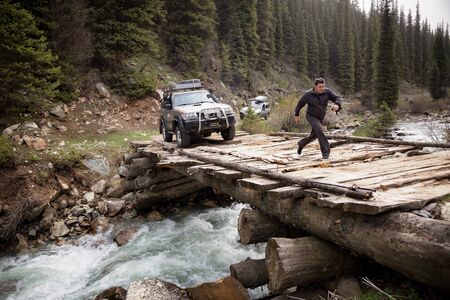 KARAKOL REGION , KYRGYZSTAN - MAY 11, 2015: Tourists come mountain river on a dilapidated wooden bridge in Tien Shan mountains, Kyrgyzstan, Central Asiaのeditorial素材