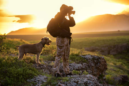 Silhouette of the photographer with a dog on background of the rising sunの写真素材
