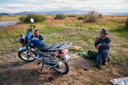 WEST MONGOLIA , MONGOLIA - AUG 04, 2011: Mongol traveling with his wife on a motorcycle stopped by the roadside to shave.のeditorial素材