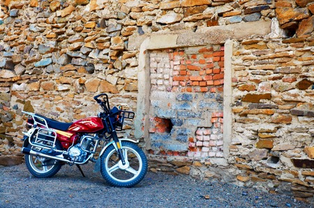 WESTERN MONGOLIA , MONGOLIA - AUG 5, 2011: Red motorbike parked near a deaf stone wall. Motorbike - the most popular transportation in modern Mongolia.のeditorial素材