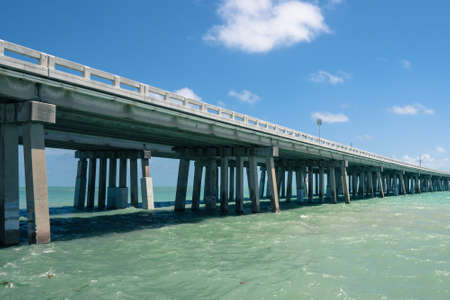 Bridge across the sea in Florida. Green water, concrete pilots, blue sky with soft clouds and speed limit sign.の写真素材