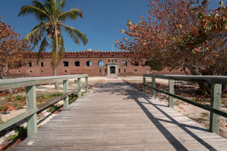Gate of an old military fort with a wooden walk in the foreground. Big brick walls and green palm trees. Fort Jefferson.の写真素材