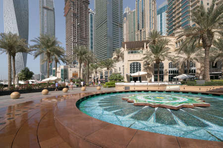 Dubai, UAE - 01.12.2019: People walking in Dubai Marina with a marble fountain in the foregound and skyscrapers in the back.のeditorial素材