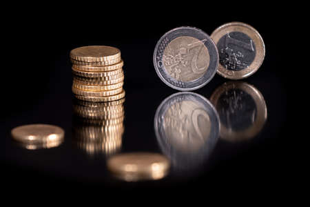 Euro coins isolated with pitch black background, reflecting in black metallic surface. Money on a...