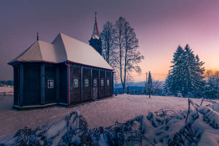Virgin Mary Church in Grun, Beskid Mountains. Beautiful small wooden church. Winter fairytale picture. Sky glows on the distant horizon.の写真素材