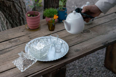 Pouring traditional Iranian tea. White teapot, crystal sugar, plate on a wooden table outdoors. Shiraz, Iran.の写真素材