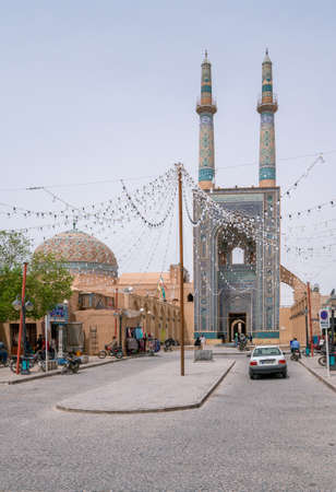 Yazd, Iran - 13.04.2019: Jameh Mosque of Yazd with its tall minarets and turquoise tiles. People walking in the street. Persia.のeditorial素材