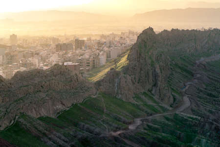 City of Qom, Iran, in a dramatic sunset viewed from the hill nearby. Steep rock cliffs in the front. Desert rocks, dramatic terrain.の写真素材