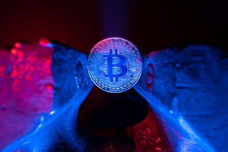 Bitcoin mounted in a steel vise in red and blue light. Keeping Bitcoin safe in crypto wallet. Pressure on crypto currency. Crypto currency restrictions. Investing instruments.の写真素材
