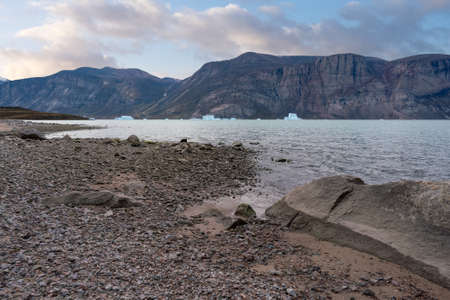 Late afternoon with soft clouds in the valley of Akshayuk pass, Baffin Island. Icebergs floating in the ocean of north Pangnirtung fjord. Harsh, remote arctic wilderness.の写真素材